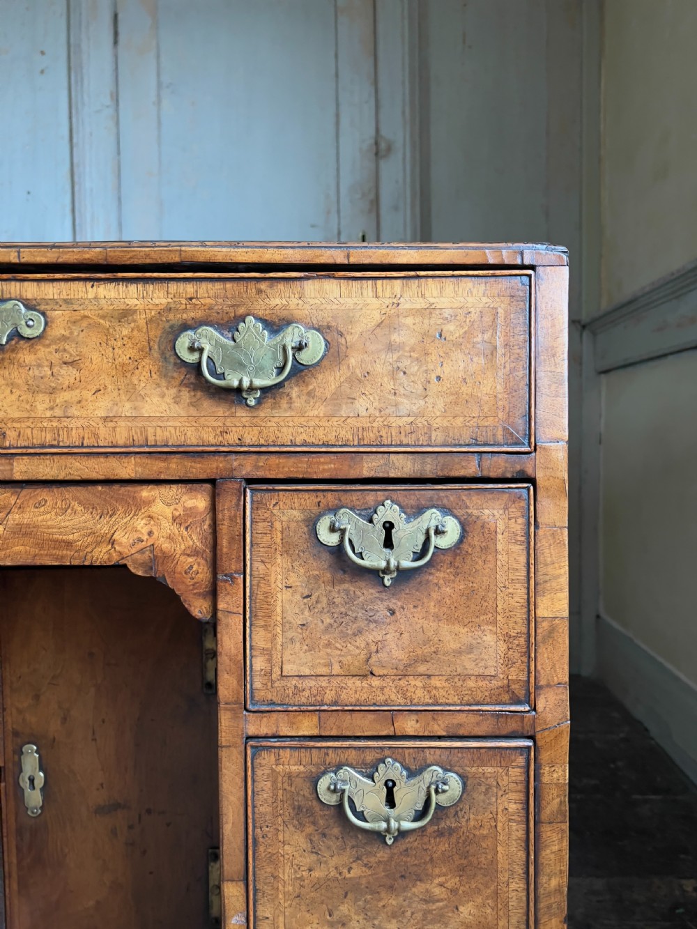 An 18th-century George II burr walnut kneehole desk featuring multiple drawers with brass handles, a central recessed cupboard, and bracket feet. View V