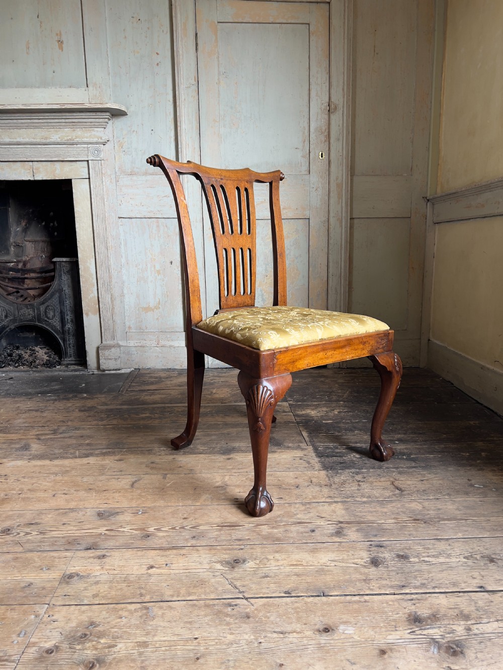 A George II period walnut side chair featuring a carved splat back, yellow damask seat cushion, and cabriole legs with claw-and-ball feet.