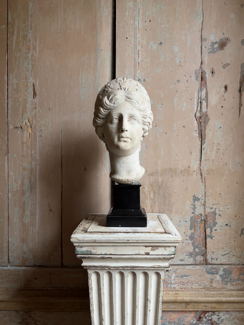 A carved marble classical bust depicting the head of Juno with wavy hair under a diadem crown, mounted on a square black pedestal.