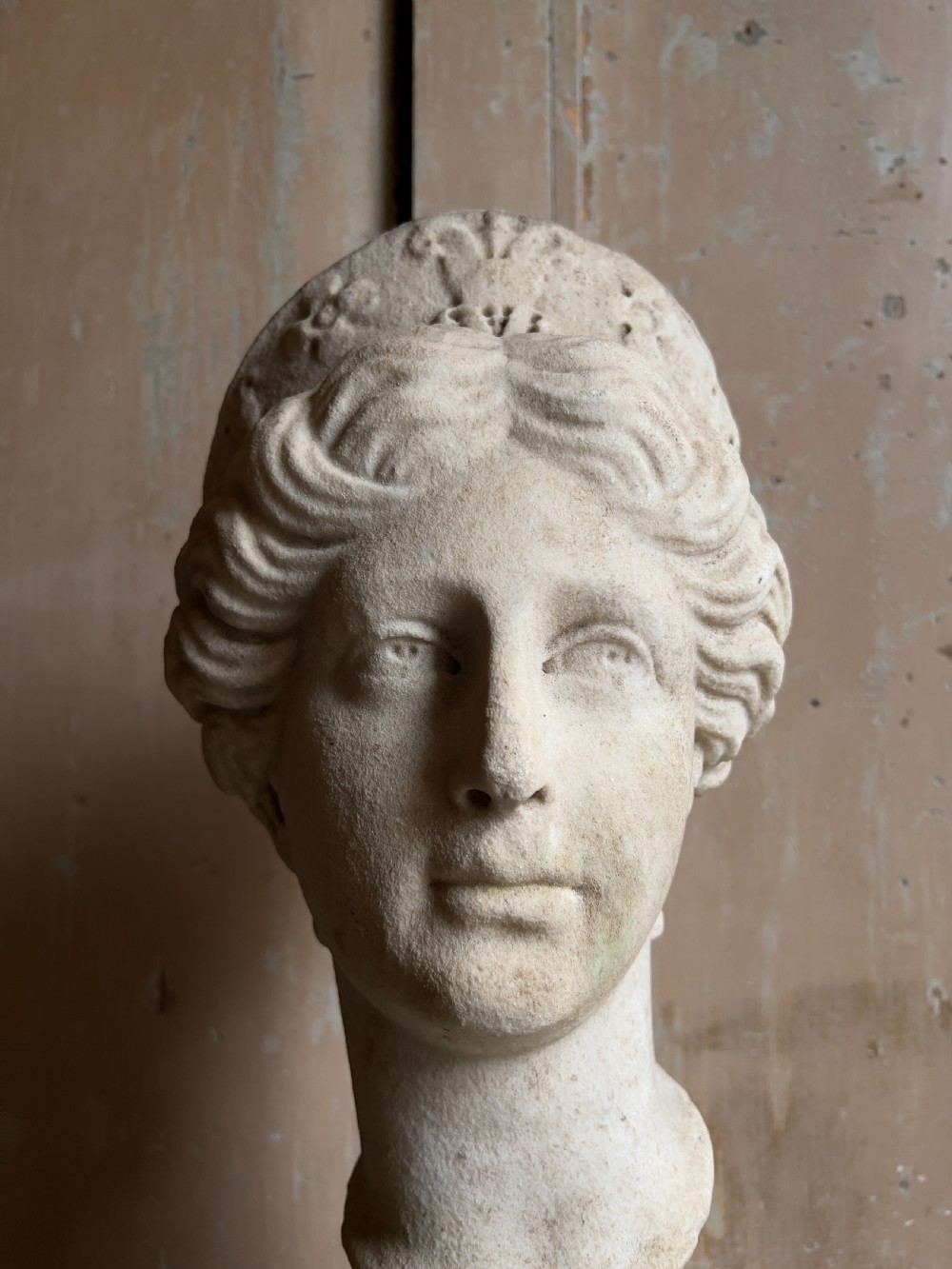 A carved marble classical bust depicting the head of Juno with wavy hair under a diadem crown, mounted on a square black pedestal. View II