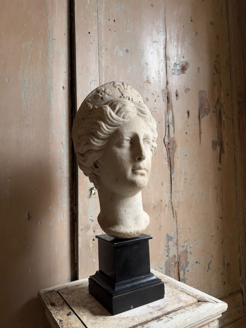 A carved marble classical bust depicting the head of Juno with wavy hair under a diadem crown, mounted on a square black pedestal. View III