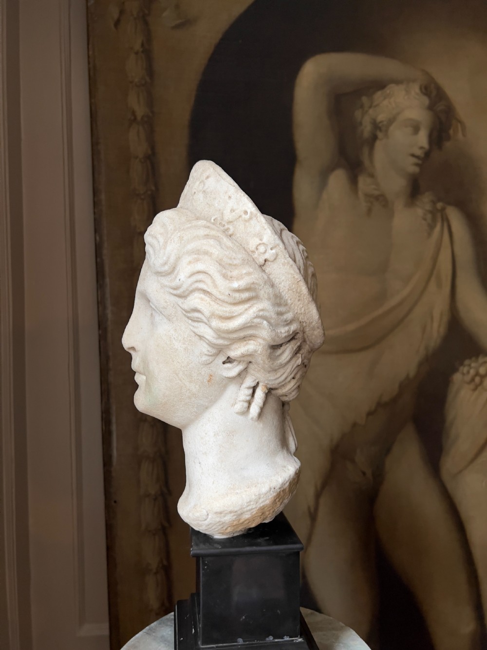 A carved marble classical bust depicting the head of Juno with wavy hair under a diadem crown, mounted on a square black pedestal. View V