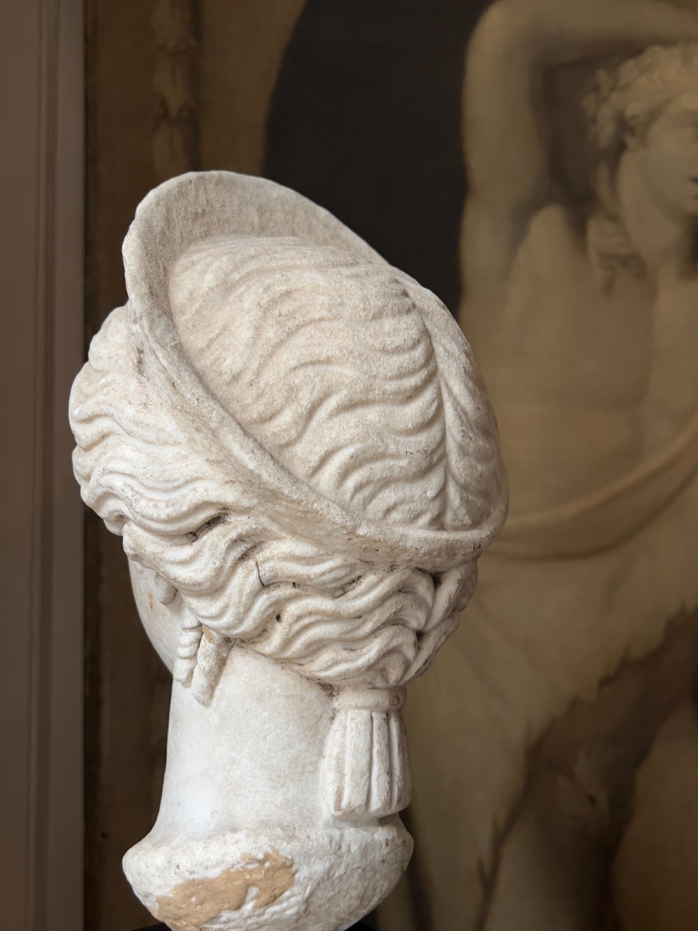 A carved marble classical bust depicting the head of Juno with wavy hair under a diadem crown, mounted on a square black pedestal. View VI