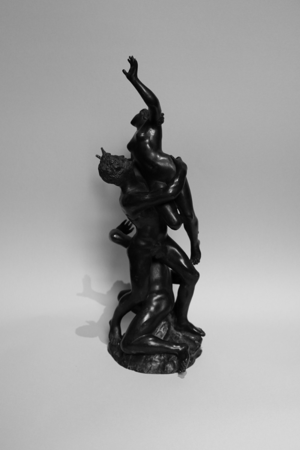 A dark patinated bronze sculpture featuring three classical interlocking figures standing in a vertical composition. View IV