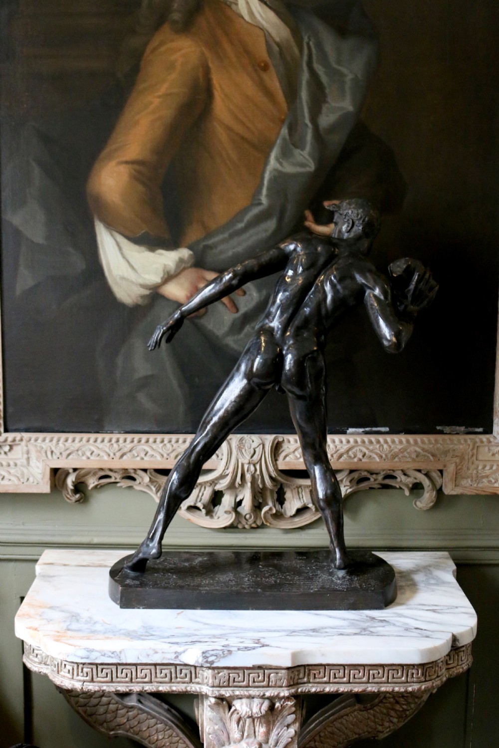A dark patinated bronze sculpture depicting a nude male athlete poised dynamically while preparing to put a stone. View IV