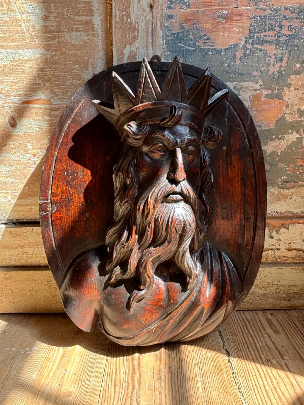 An 18th-century carved dark wood oval plaque featuring a high-relief depiction of Neptune wearing a spiked crown.
