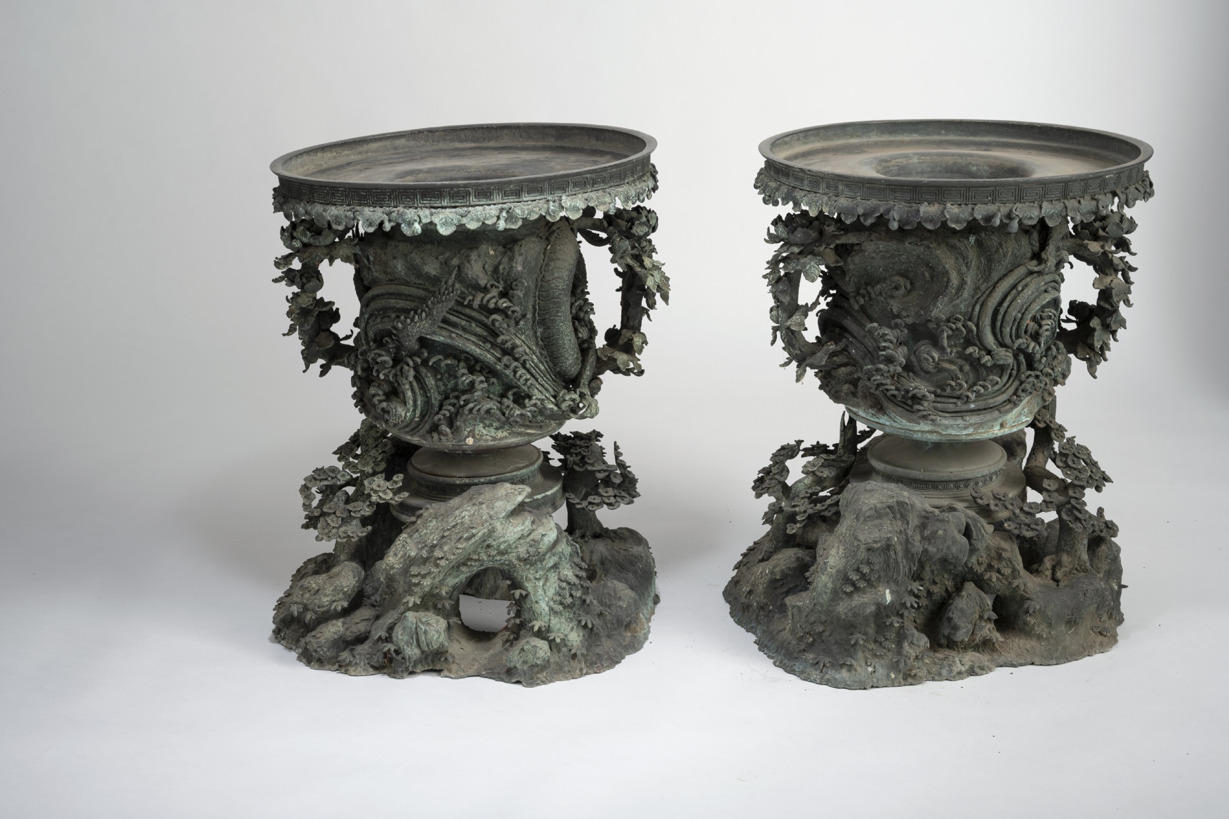 A pair of large, intricately cast Japanese bronze garden urns featuring relief-carved dragons, foliage, and naturalistic grotto-style bases with a verdigris patina. View III