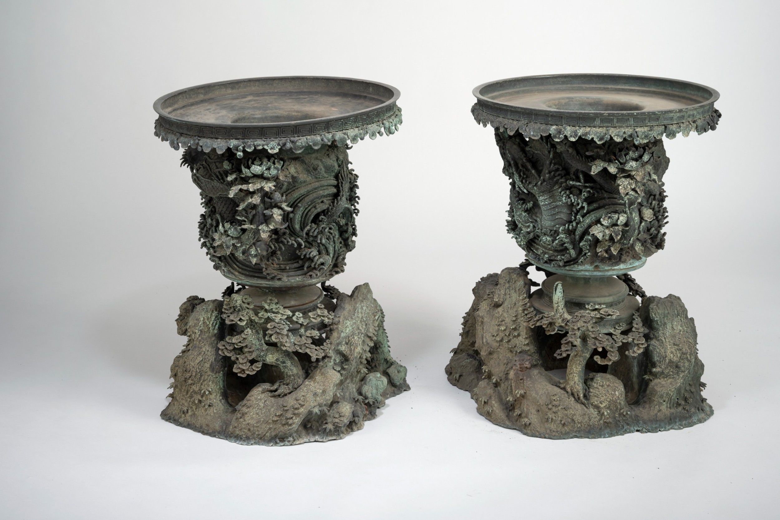 A pair of large, intricately cast Japanese bronze garden urns featuring relief-carved dragons, foliage, and naturalistic grotto-style bases with a verdigris patina. View IV
