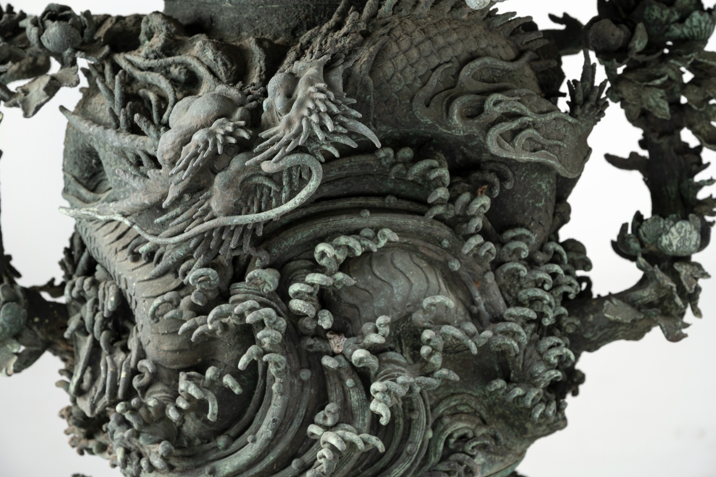 A pair of large, intricately cast Japanese bronze garden urns featuring relief-carved dragons, foliage, and naturalistic grotto-style bases with a verdigris patina. View VI