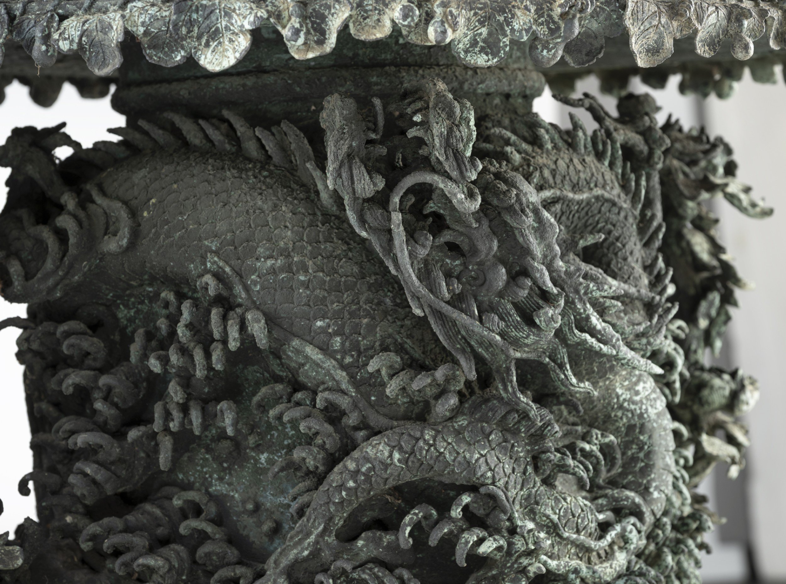 A pair of large, intricately cast Japanese bronze garden urns featuring relief-carved dragons, foliage, and naturalistic grotto-style bases with a verdigris patina. View VII