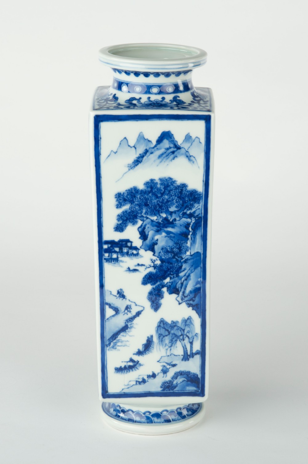 A tall quadrangular Japanese porcelain vase decorated with underglaze cobalt blue landscape scenes and geometric panels on a white ground. View II