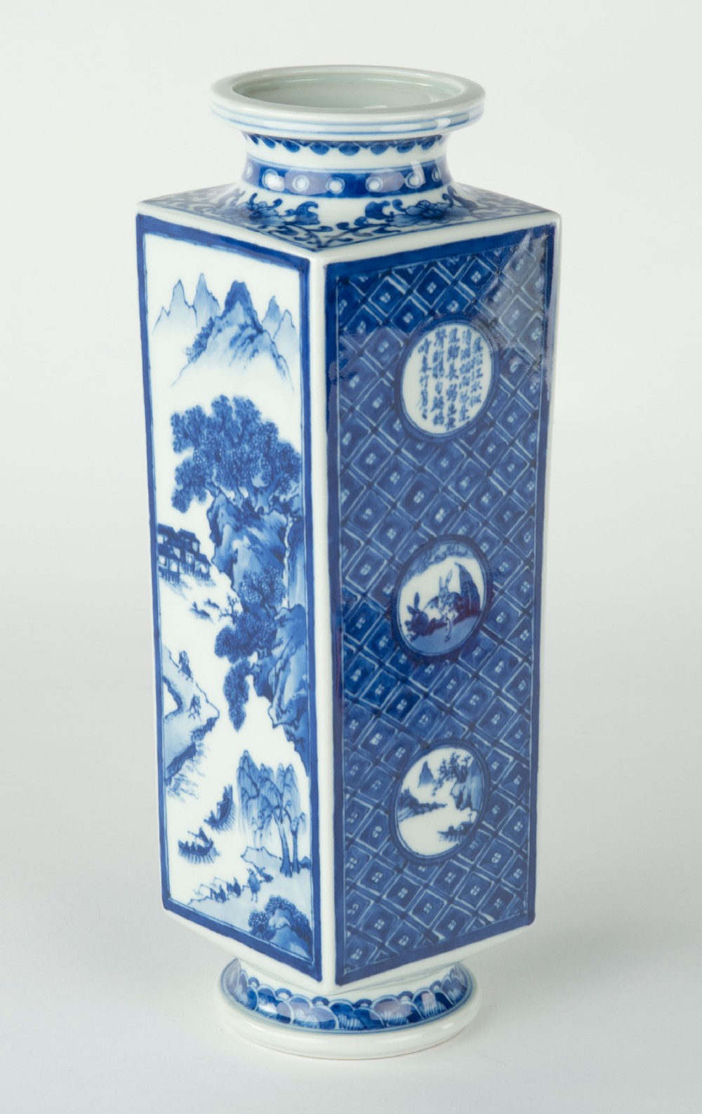 A tall quadrangular Japanese porcelain vase decorated with underglaze cobalt blue landscape scenes and geometric panels on a white ground. View III