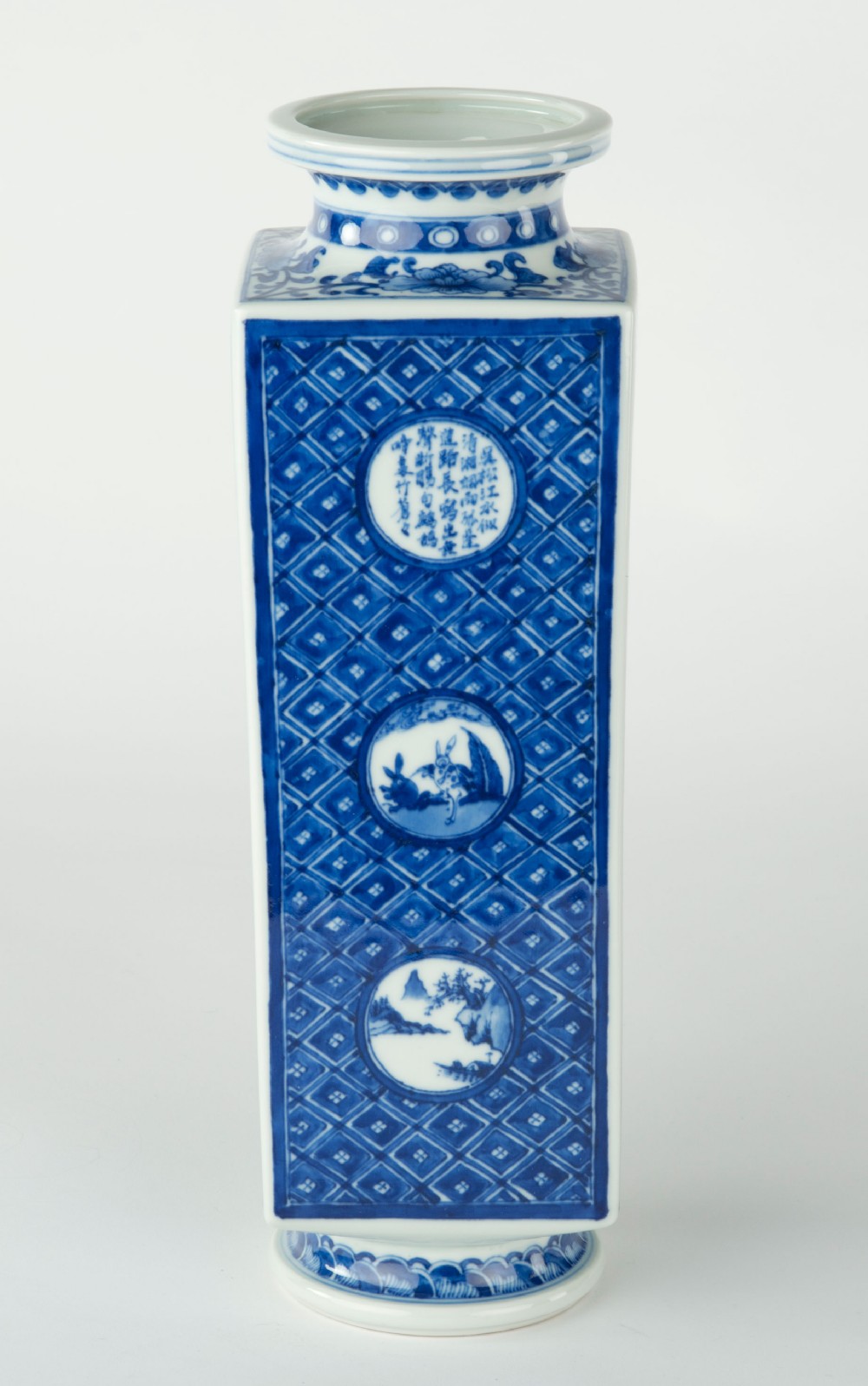 A tall quadrangular Japanese porcelain vase decorated with underglaze cobalt blue landscape scenes and geometric panels on a white ground. View IV