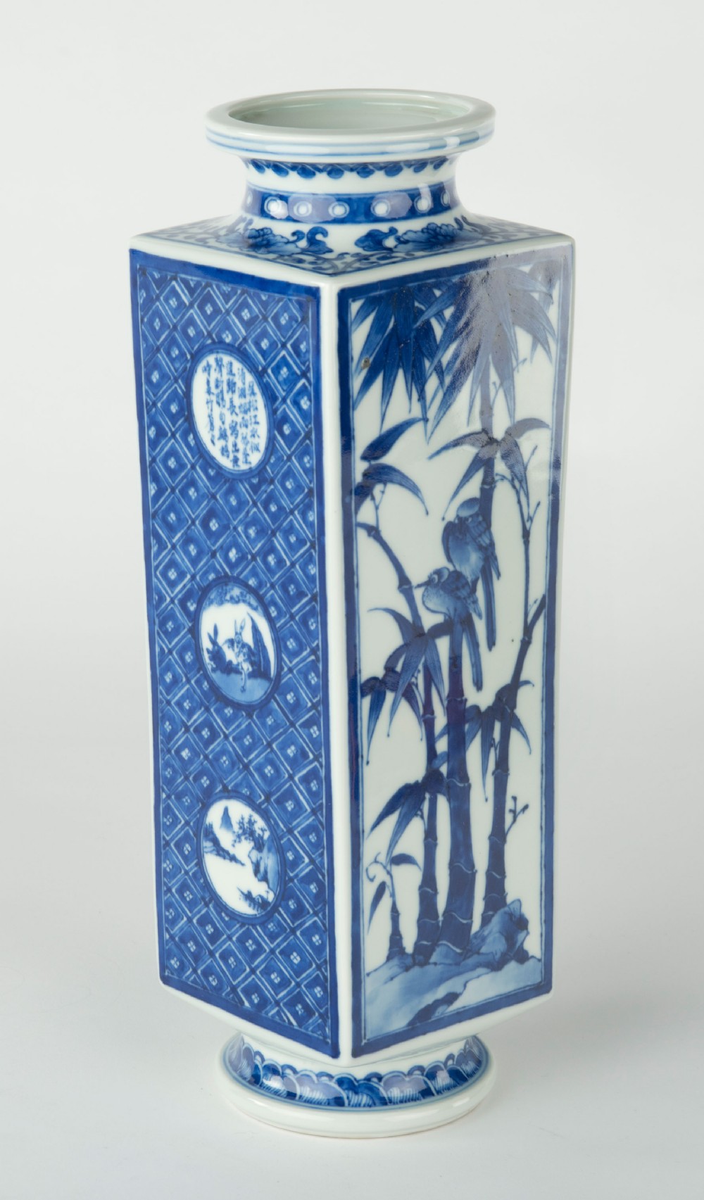 A tall quadrangular Japanese porcelain vase decorated with underglaze cobalt blue landscape scenes and geometric panels on a white ground. View V