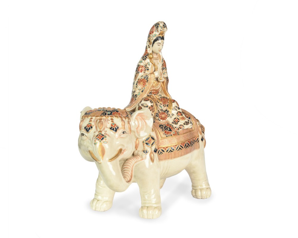 A Japanese Satsuma ceramic okimono depicting a figure adorned in elaborate polychrome robes seated atop a cream-coloured elephant with gilded accents. View III