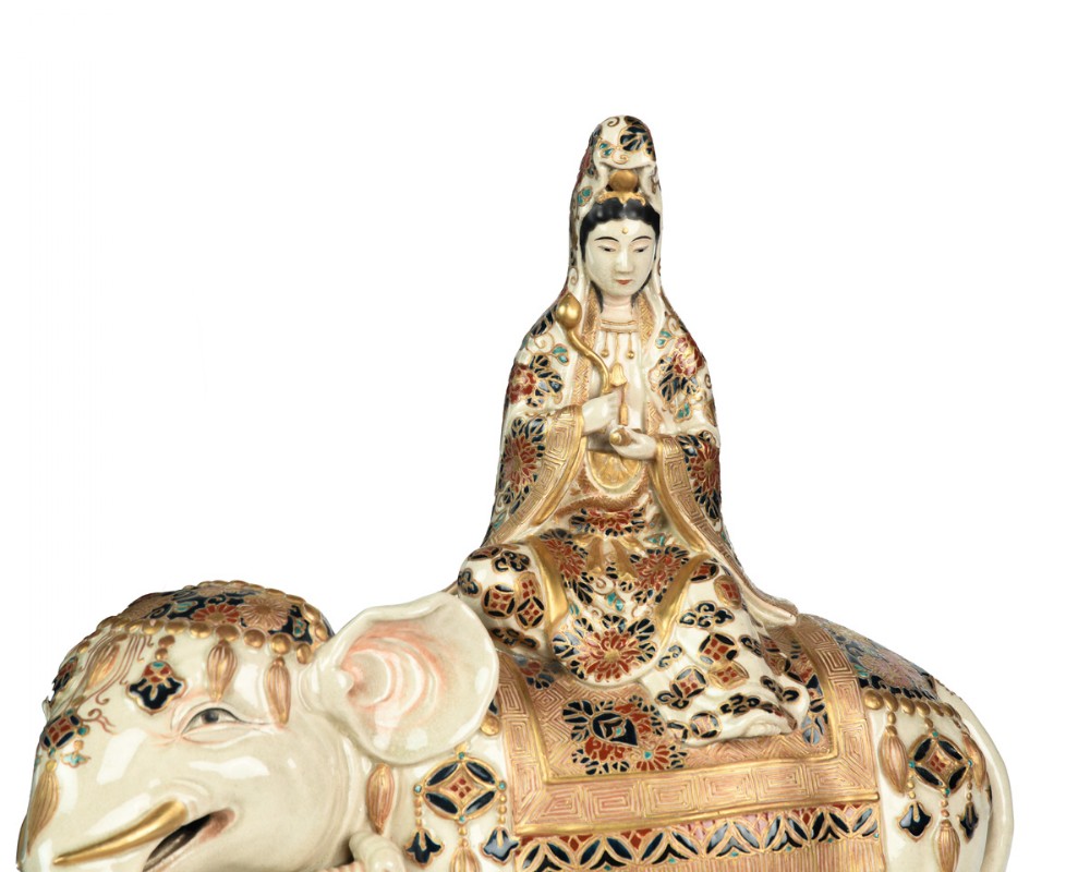 A Japanese Satsuma ceramic okimono depicting a figure adorned in elaborate polychrome robes seated atop a cream-coloured elephant with gilded accents. View VI
