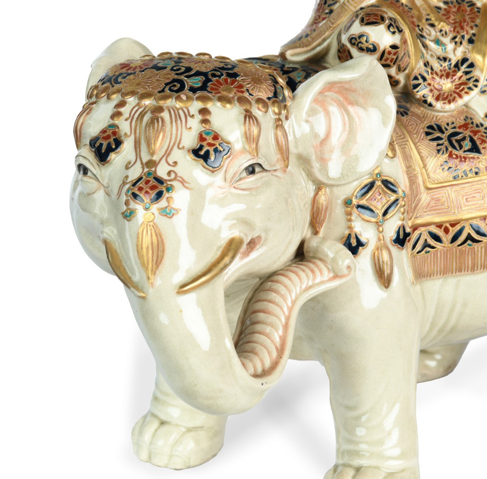 A Japanese Satsuma ceramic okimono depicting a figure adorned in elaborate polychrome robes seated atop a cream-coloured elephant with gilded accents. View VIII
