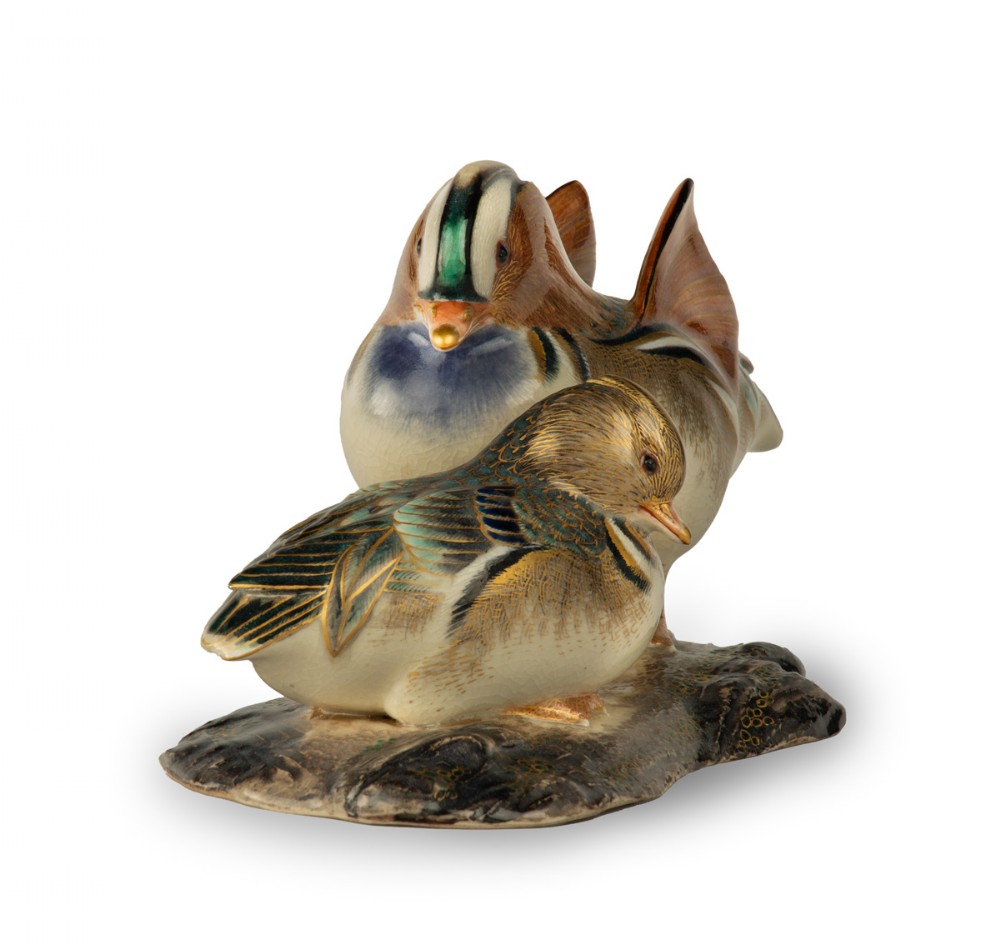 A Japanese porcelain sculpture depicting a pair of Mandarin ducks with detailed polychrome enamel feathers and gilt accents set on a dark textured base. View II