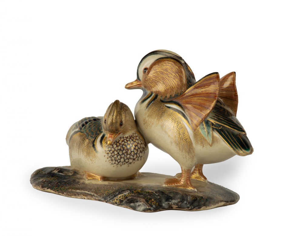 A Japanese porcelain sculpture depicting a pair of Mandarin ducks with detailed polychrome enamel feathers and gilt accents set on a dark textured base. View VI