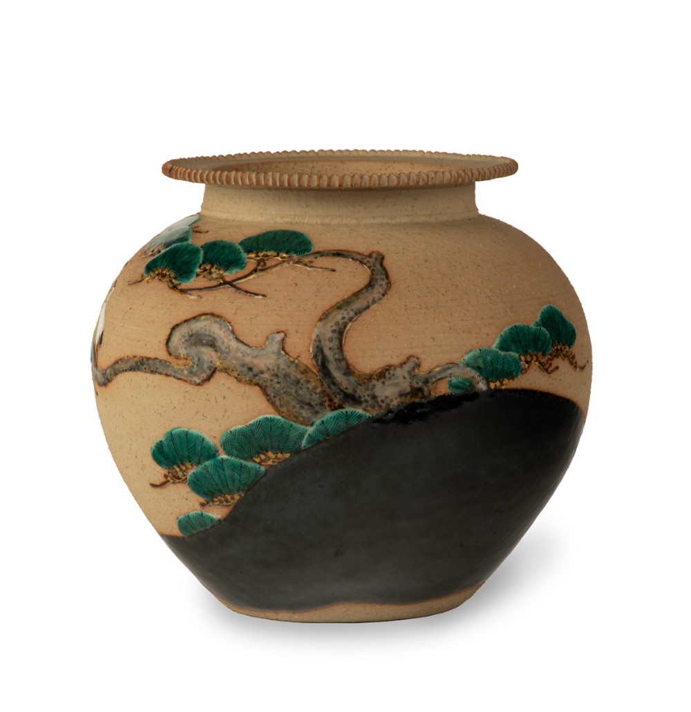 A rounded beige stoneware jardiniere decorated with high-relief green pine branches and white cranes above a black band base. View V