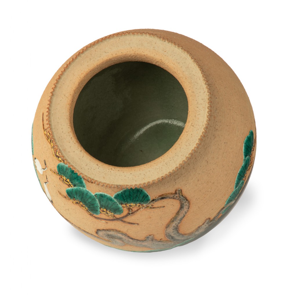 A rounded beige stoneware jardiniere decorated with high-relief green pine branches and white cranes above a black band base. View VI