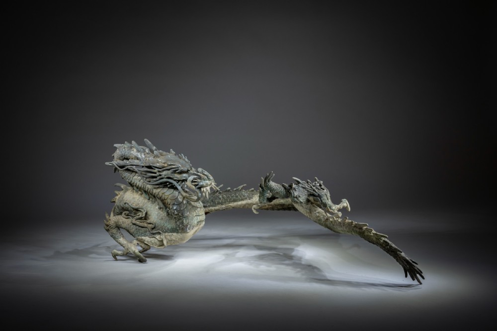 A large patinated bronze Japanese dragon sculpture with detailed chiselled scales and claws resting on a flat surface.