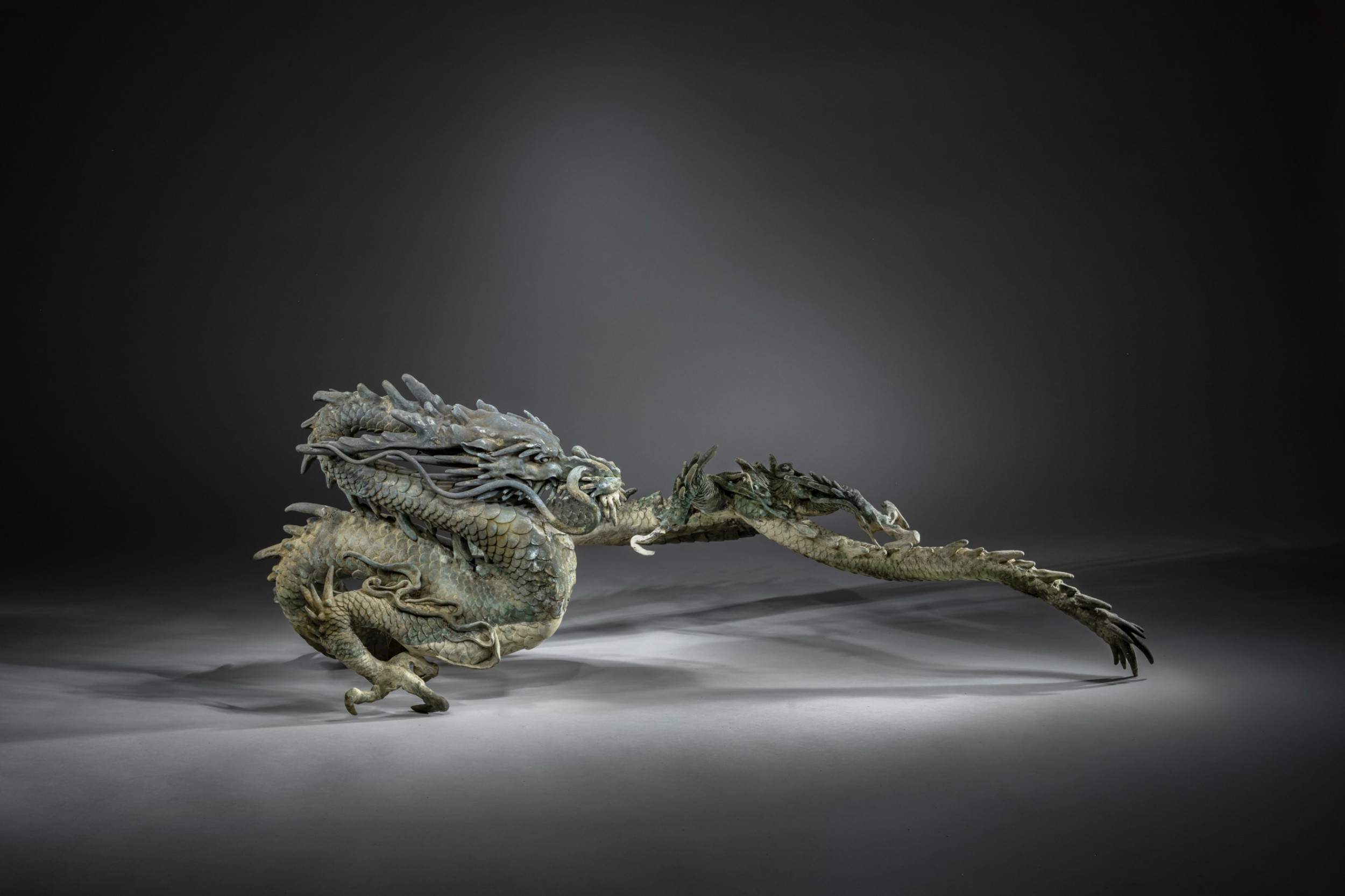 A large patinated bronze Japanese dragon sculpture with detailed chiselled scales and claws resting on a flat surface. View II