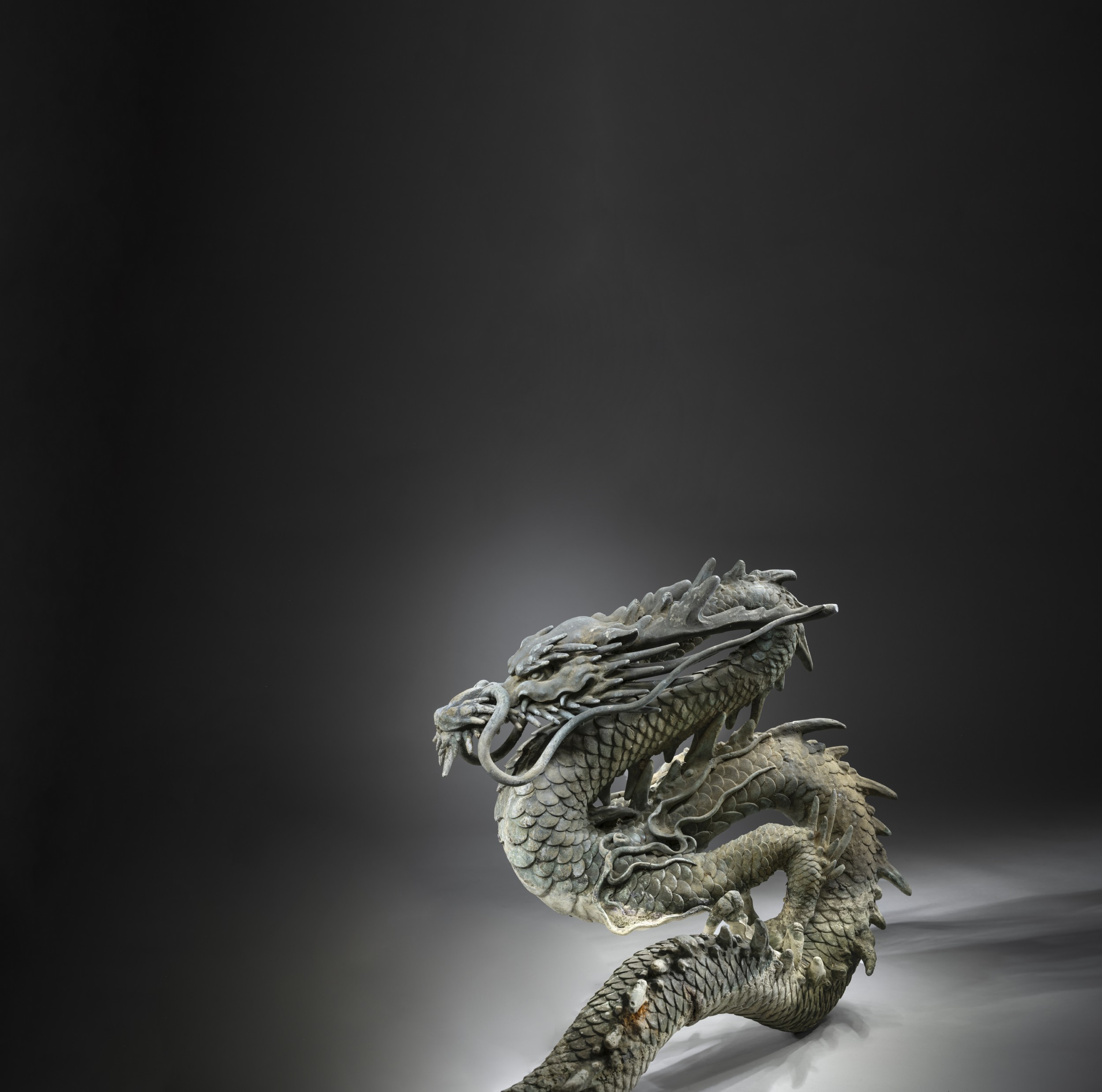 A large patinated bronze Japanese dragon sculpture with detailed chiselled scales and claws resting on a flat surface. View III