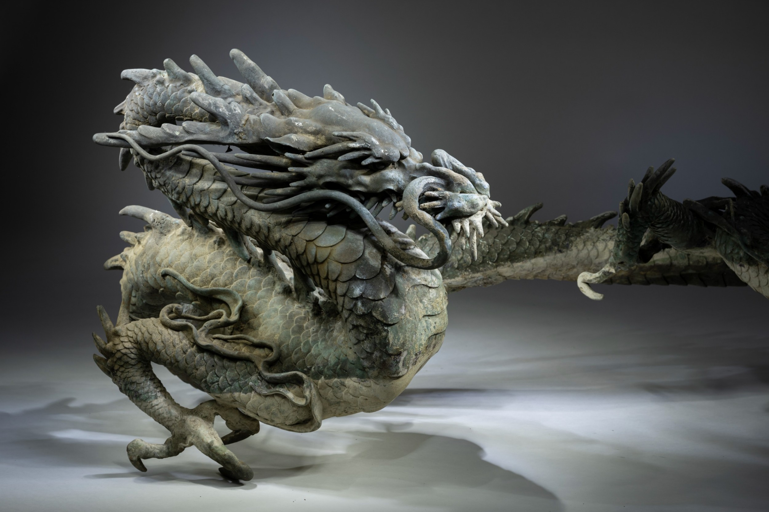 A large patinated bronze Japanese dragon sculpture with detailed chiselled scales and claws resting on a flat surface. View IV