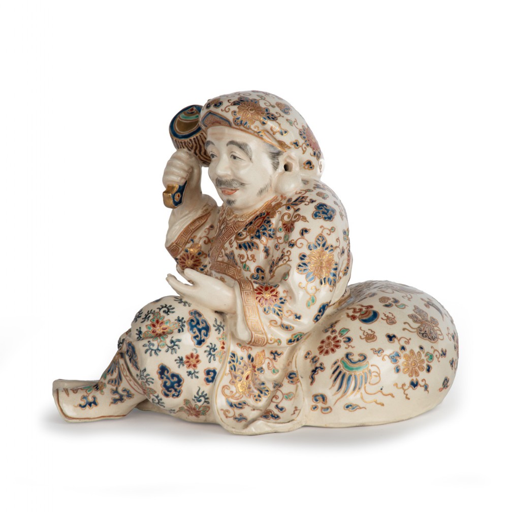A Japanese Satsuma earthenware okimono depicting the deity Daikoku seated with a mallet and sack, decorated with detailed enamels and gilding. View IV
