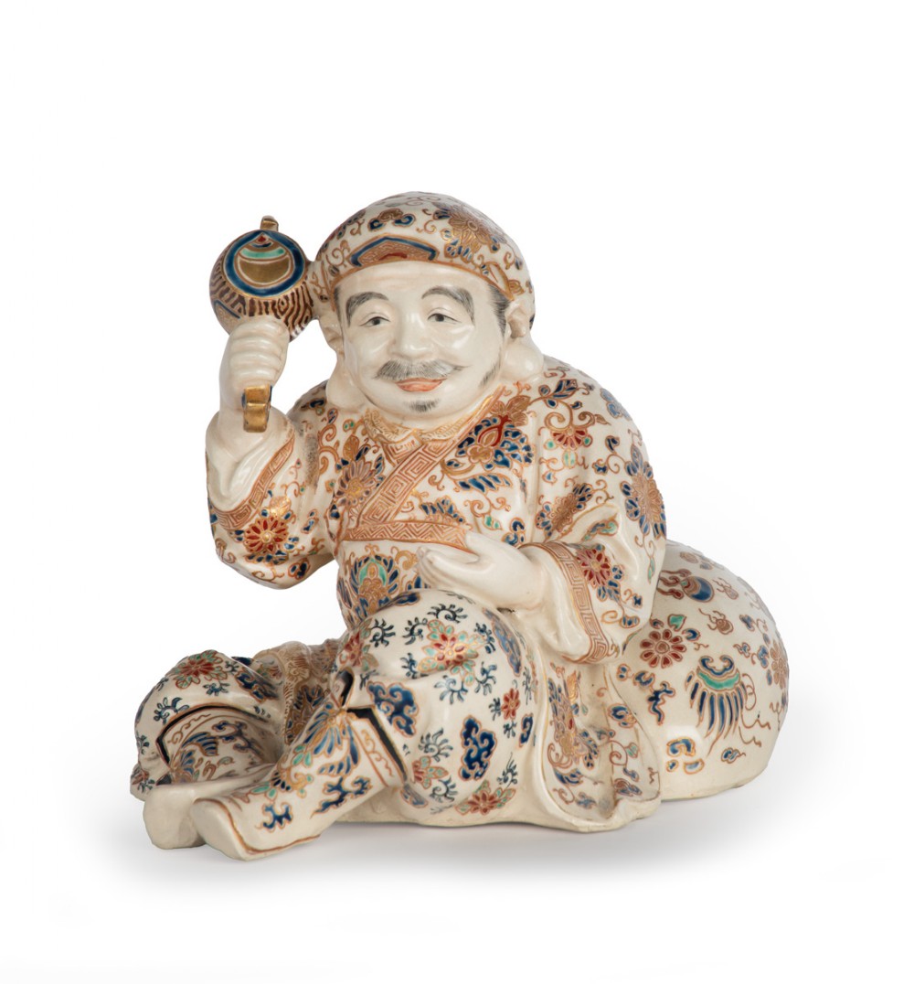 A Japanese Satsuma earthenware okimono depicting the deity Daikoku seated with a mallet and sack, decorated with detailed enamels and gilding. View VI