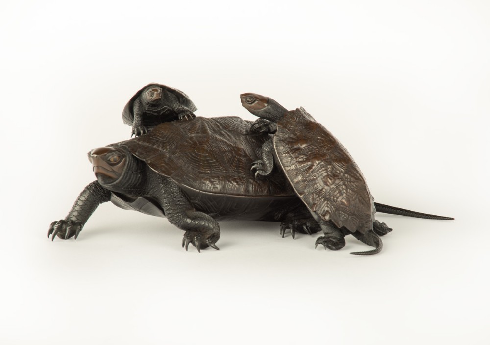 A Japanese bronze sculpture depicting a large turtle with two smaller turtles crawling on its shell.