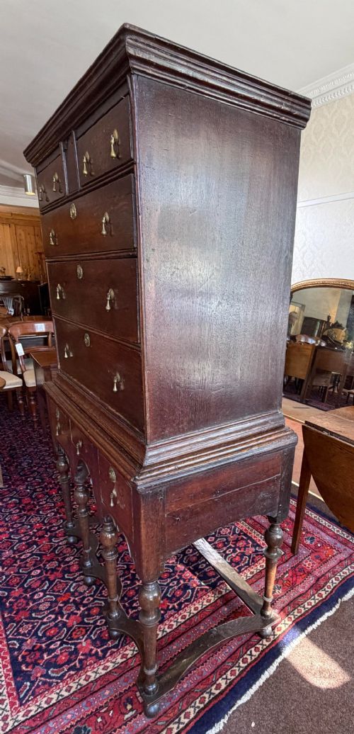 A mid 18th century dark oak chest on stand featuring multiple drawers, brass drop handles, a shaped lower apron, and turned legs with stretchers. View II