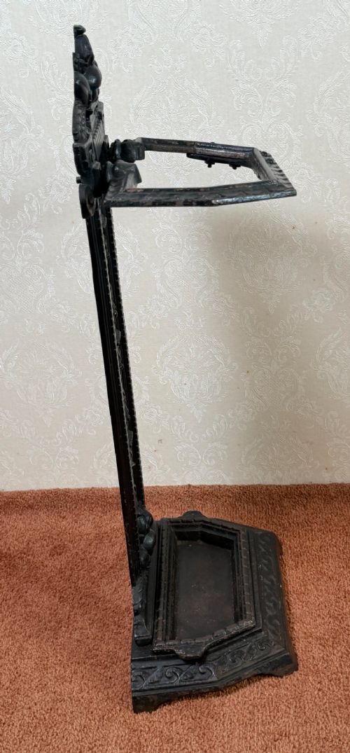 A Victorian black cast iron umbrella stand featuring a foliate crest, an openwork backplate, a retaining rail, and a drip tray base. View III