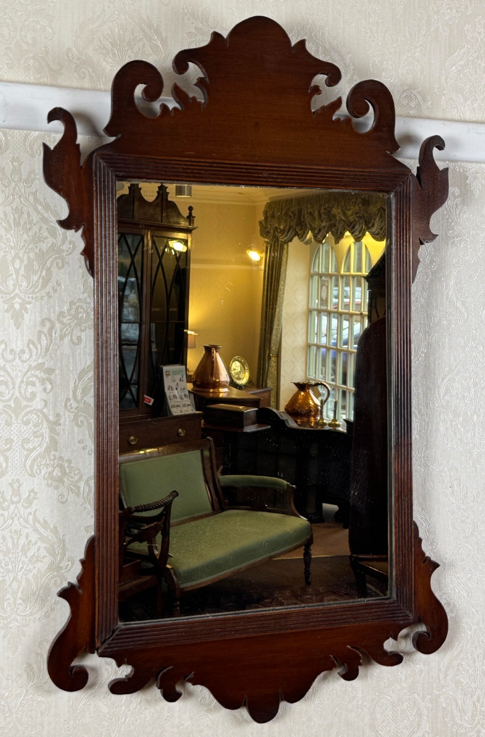 A mahogany Chippendale style wall mirror featuring intricate fretwork scrollwork on the top crest and bottom apron.