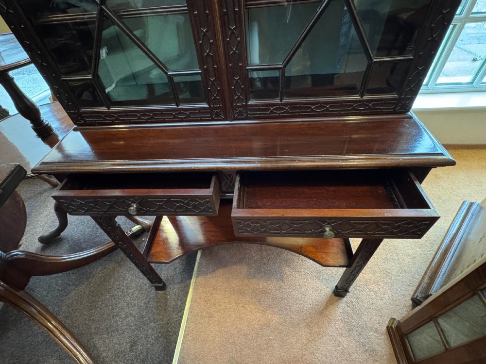 A Chippendale style dark mahogany display cabinet featuring a broken pediment top, geometric astragal glazed double doors, blind fretwork carving, and a lower shelf on square legs. View II