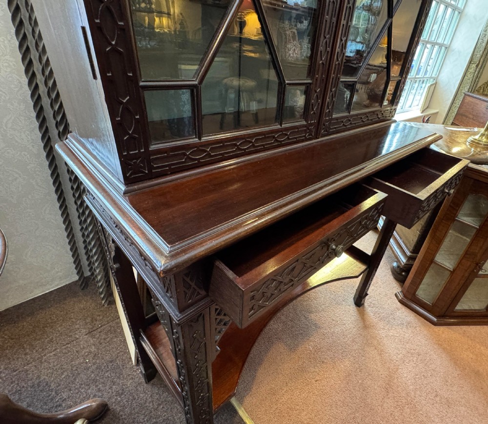 A Chippendale style dark mahogany display cabinet featuring a broken pediment top, geometric astragal glazed double doors, blind fretwork carving, and a lower shelf on square legs. View III