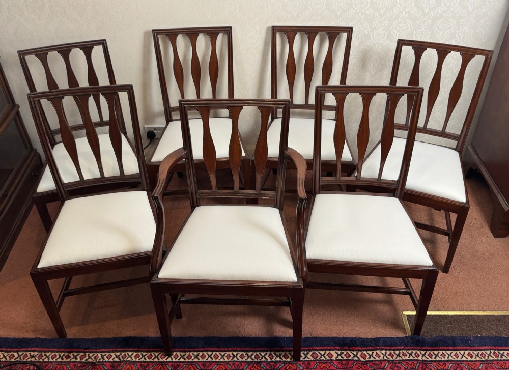 A set of seven mahogany dining chairs with carved vertical splat backs, including six side chairs and one carver armchair with cream fabric seats.