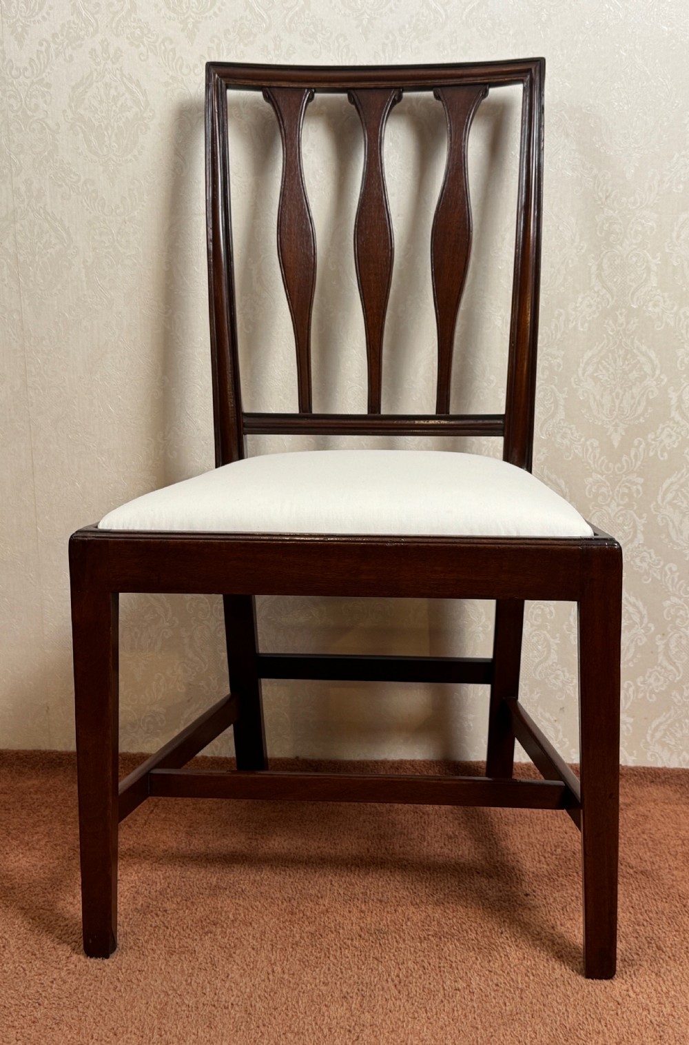 A set of seven mahogany dining chairs with carved vertical splat backs, including six side chairs and one carver armchair with cream fabric seats. View VI