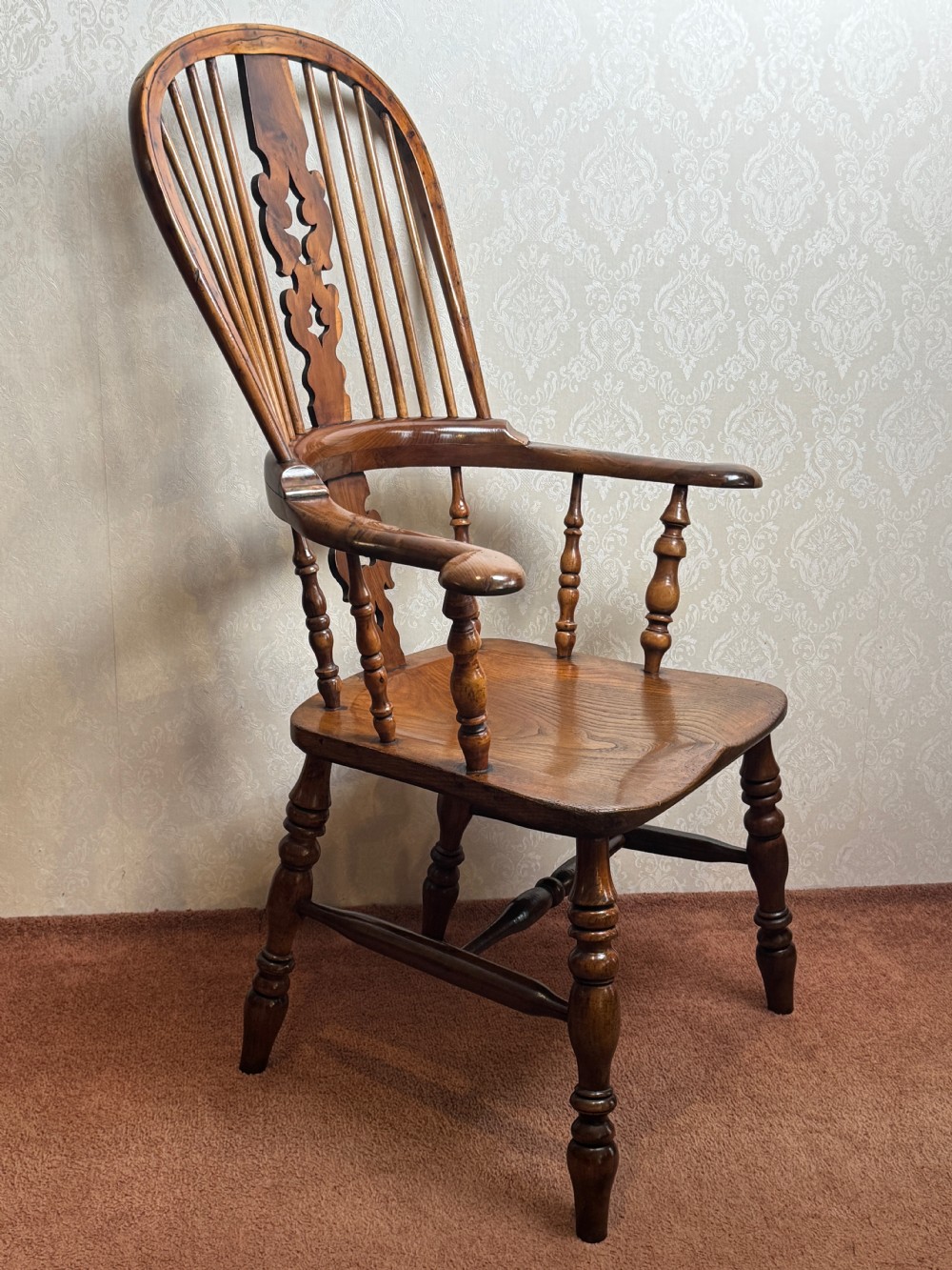 A high back yew wood Windsor armchair featuring an arched hoop back, a pierced central splat, broad curved arms, and turned wooden legs.