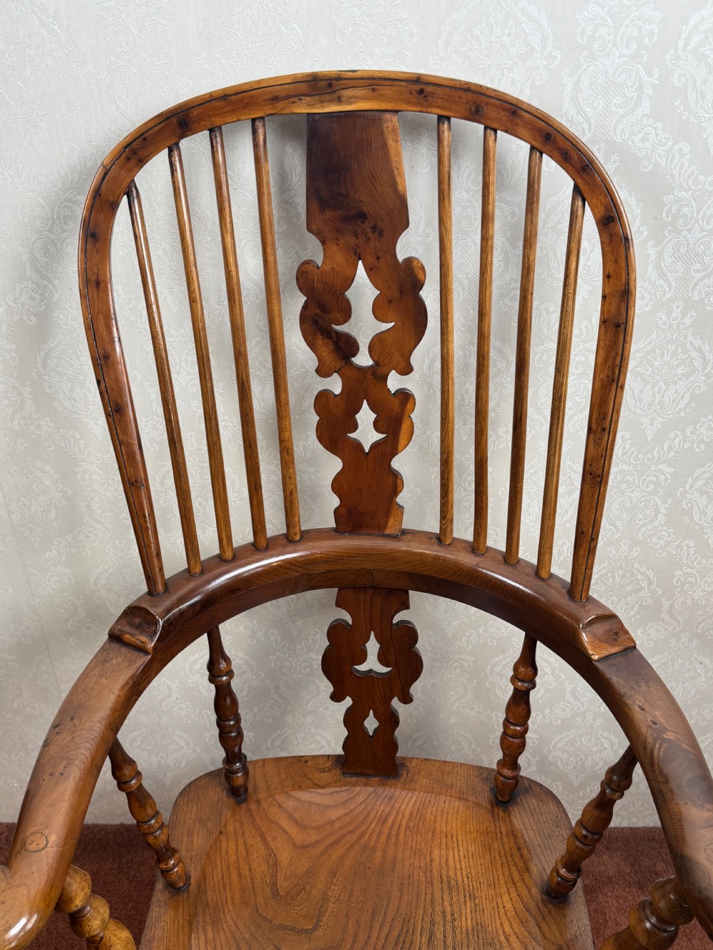 A high back yew wood Windsor armchair featuring an arched hoop back, a pierced central splat, broad curved arms, and turned wooden legs. View V