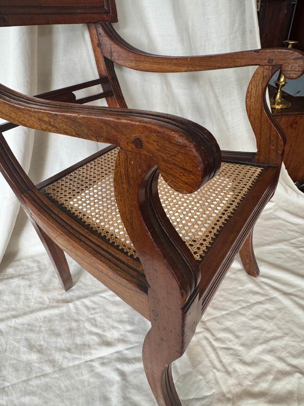 A Regency period mahogany childs armchair featuring a woven cane seat, sweeping armrests, panelled top rail, and curved sabre legs. View II