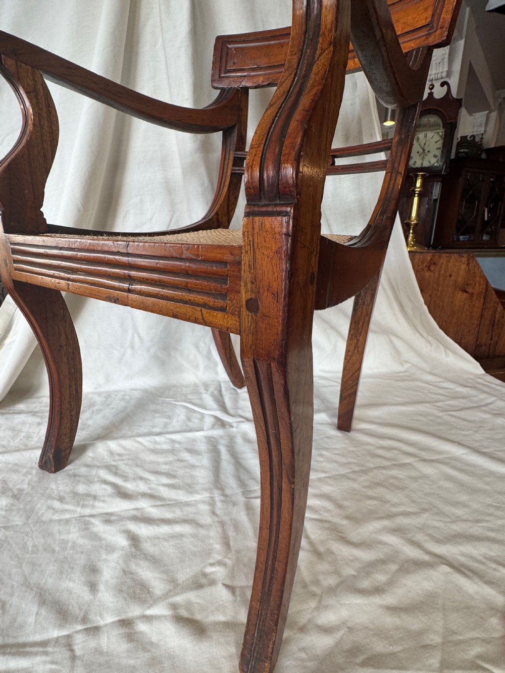 A Regency period mahogany childs armchair featuring a woven cane seat, sweeping armrests, panelled top rail, and curved sabre legs. View IV