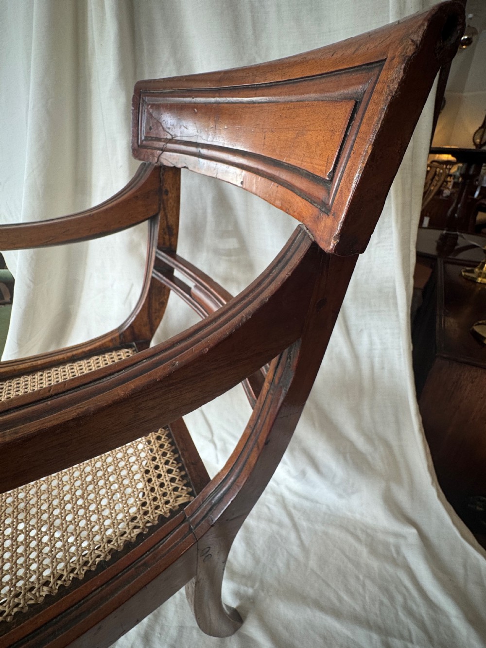 A Regency period mahogany childs armchair featuring a woven cane seat, sweeping armrests, panelled top rail, and curved sabre legs. View VII
