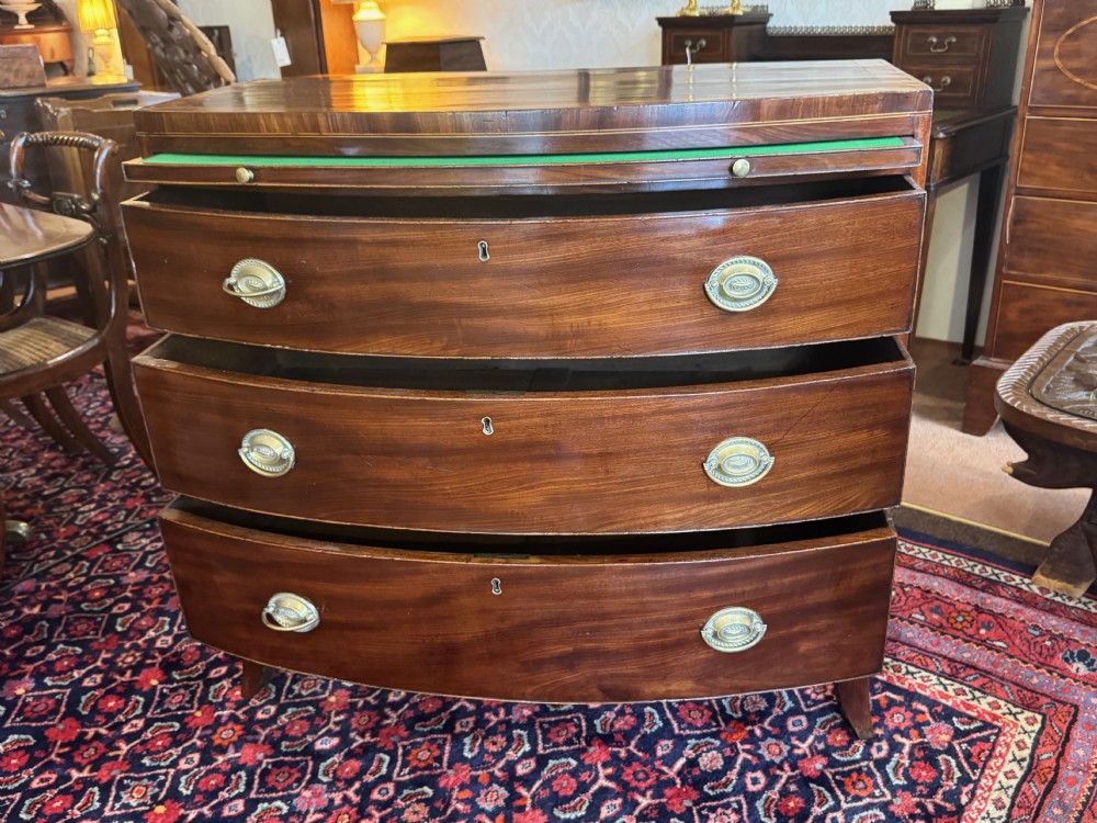 An antique Georgian mahogany bowfront chest featuring three drawers, a upper brushing slide, brass oval handles, and splayed bracket feet. View II