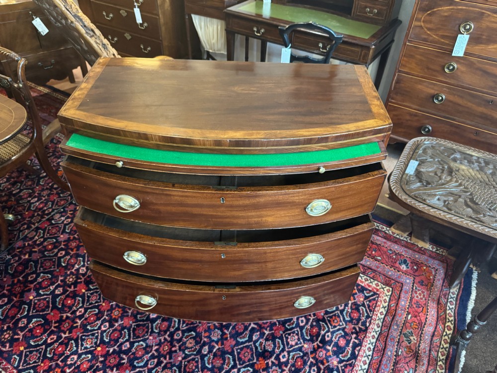 An antique Georgian mahogany bowfront chest featuring three drawers, a upper brushing slide, brass oval handles, and splayed bracket feet. View III