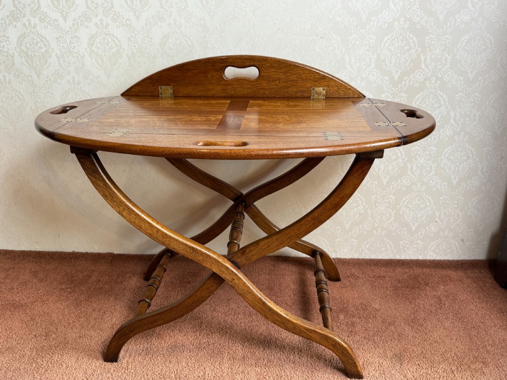 An early nineteenth-century wooden butler tray table featuring a hinged oval top with cutout handles resting on a curved folding X-frame base.