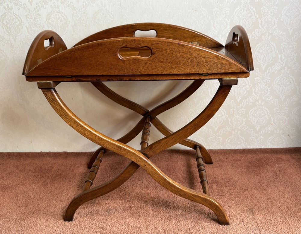 An early nineteenth-century wooden butler tray table featuring a hinged oval top with cutout handles resting on a curved folding X-frame base. View II