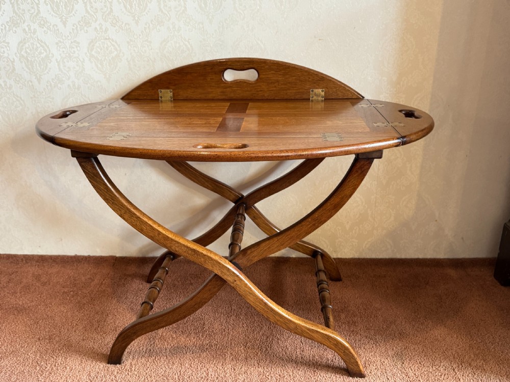 An early nineteenth-century wooden butler tray table featuring a hinged oval top with cutout handles resting on a curved folding X-frame base. View III