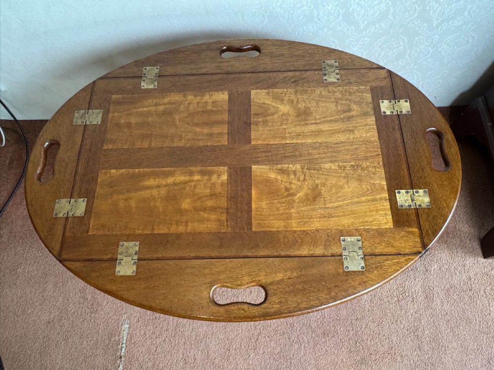 An early nineteenth-century wooden butler tray table featuring a hinged oval top with cutout handles resting on a curved folding X-frame base. View V